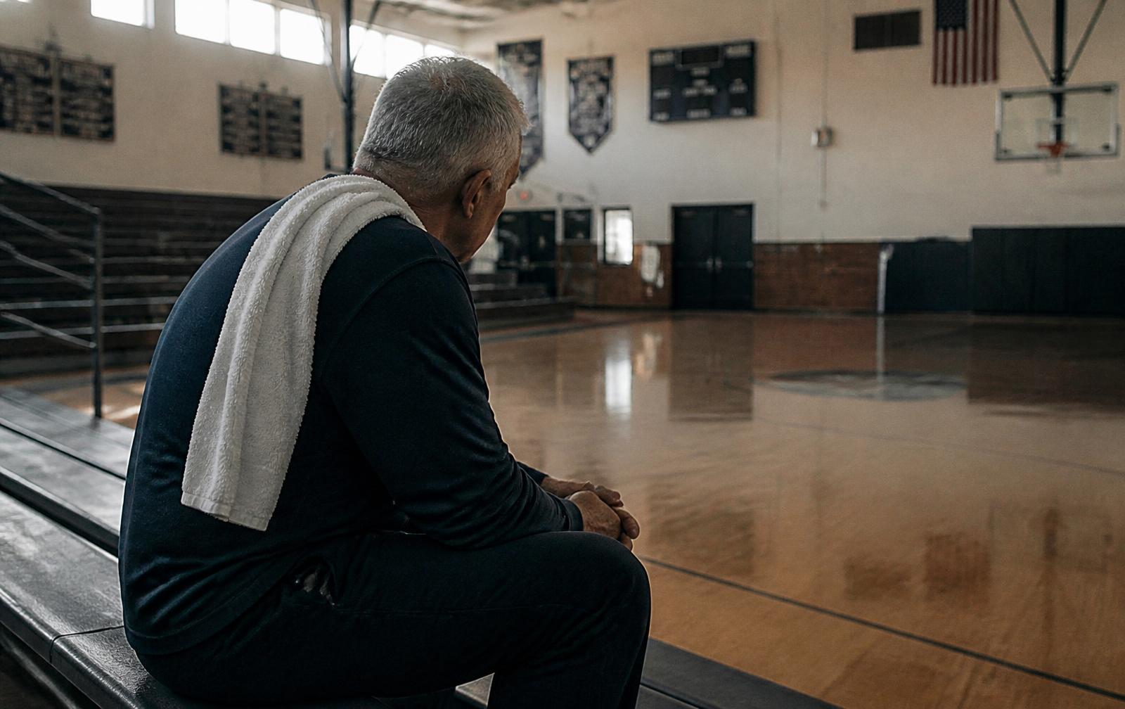 A coach sitting alone on the bleachers in an empty gymnasium after practice