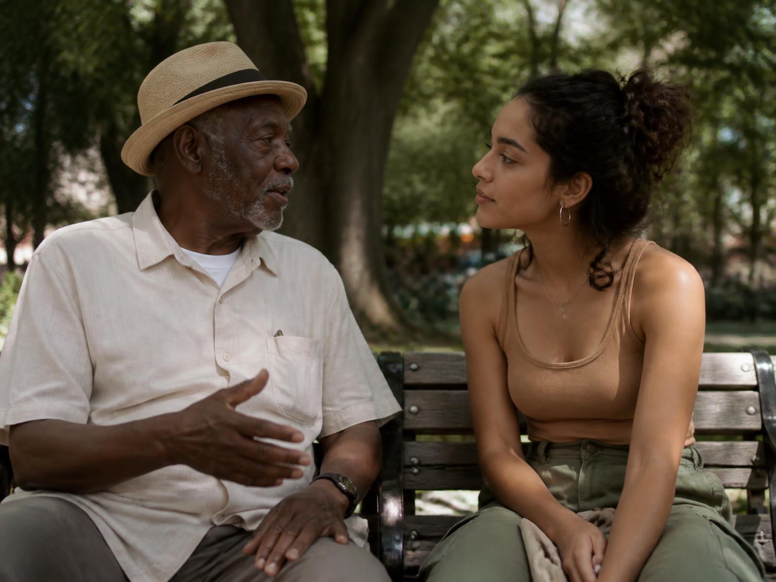 An older man and a young woman sitting side by side on a park bench mid-conversation