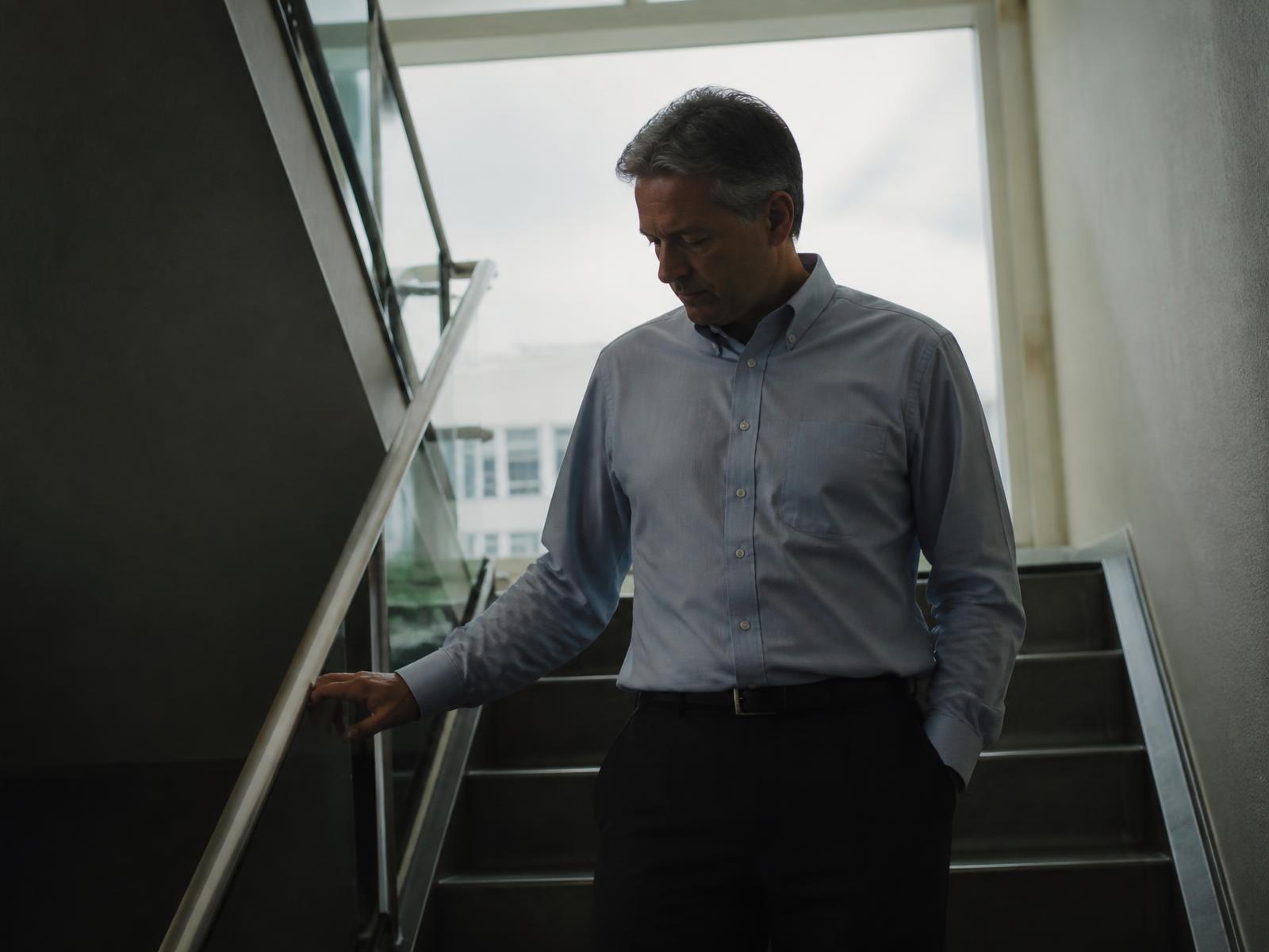 A man pausing on an office stairwell landing between meetings