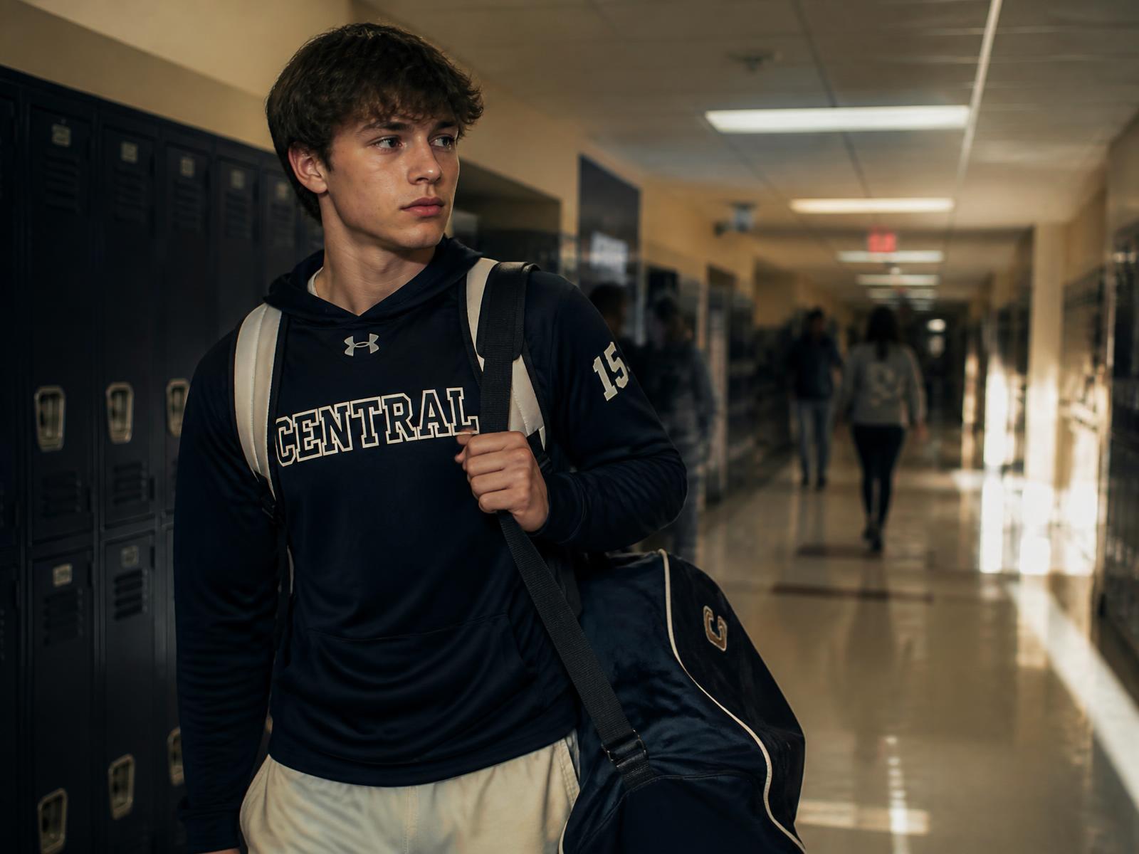 A student athlete carrying a backpack and sports bag through a school hallway
