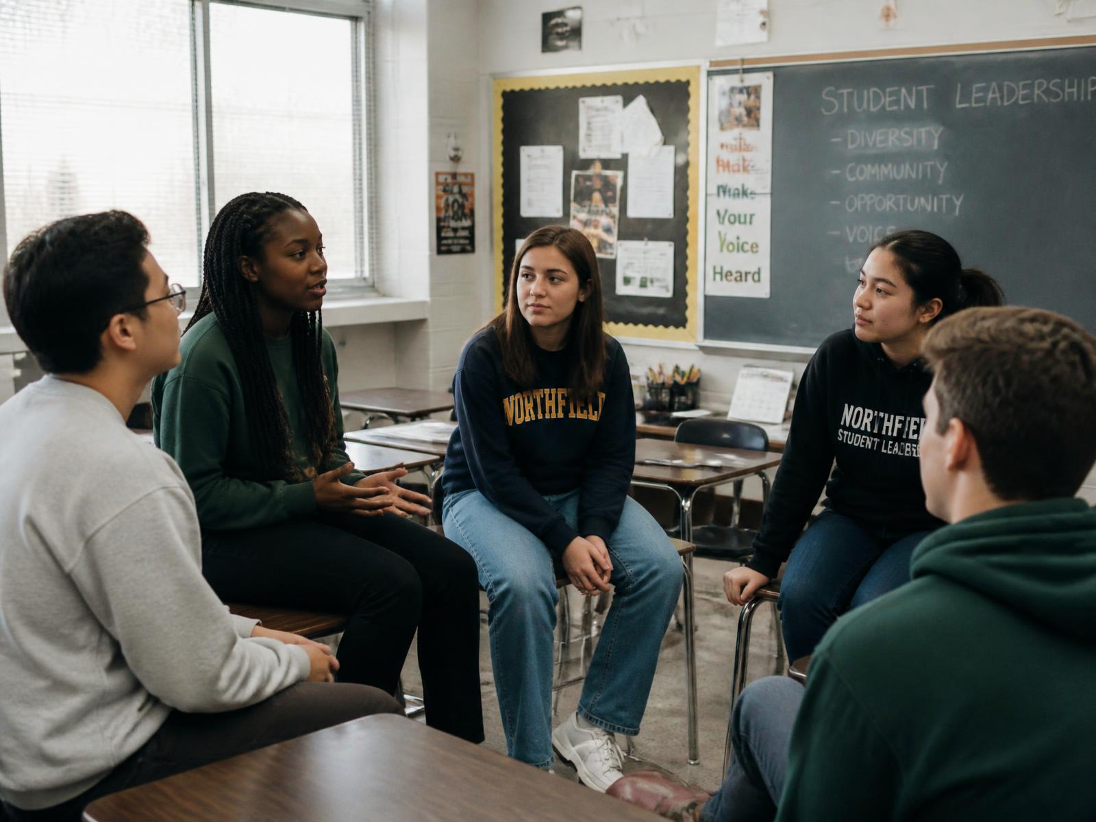 A small circle of student leaders talking together in a classroom after school