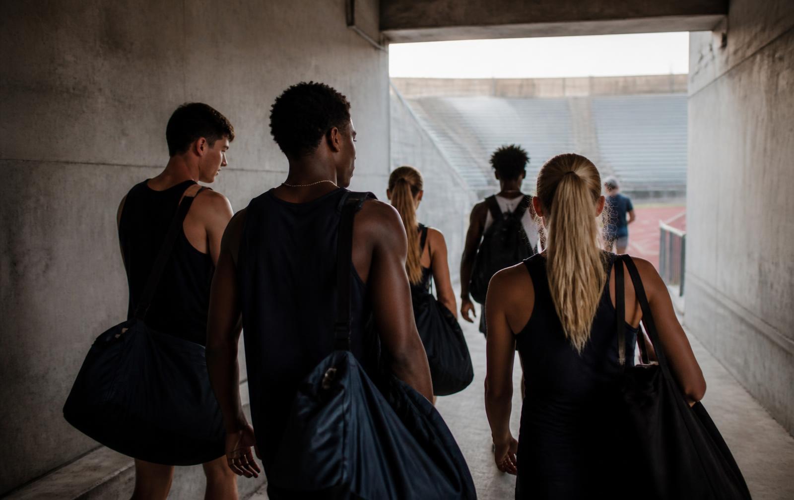 Track athletes walking together through a stadium tunnel after practice