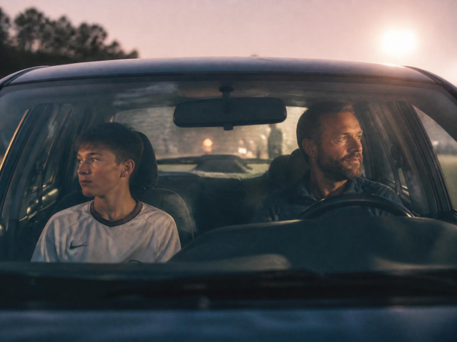 A father and his teenage son sitting quietly in a car after a soccer game